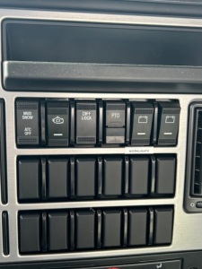 Dashboard switches and controls on a new Mack MD7 truck showing multiple labeled buttons such as MUD/SNOW, DIFF LOCK, PTO, and ATC OFF.
