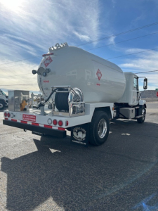 Vehicle rear view of a tanker truck with hose reel, cylindrical tank, and hazard placards.