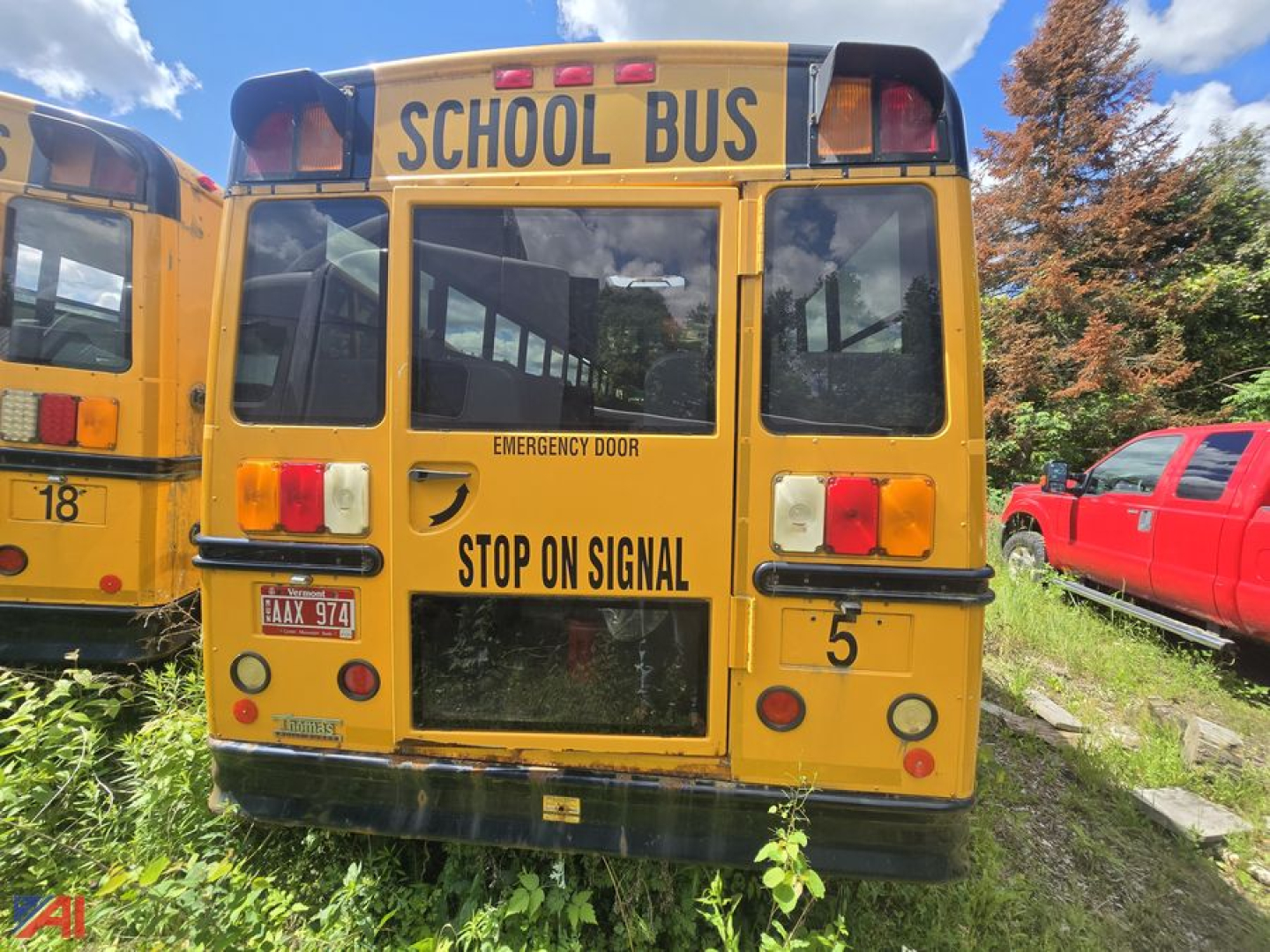 Back view of a yellow school bus with STOP ON SIGNAL text and emergency door label, letters SCHOOL BUS across top, red taillights, rear windows, license plate visible.