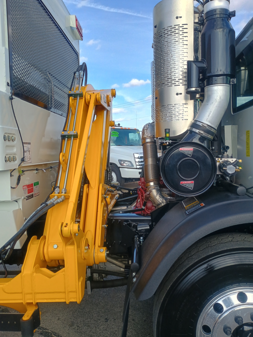Truck side showing yellow front loader arm attached to a Mack LR64, with chrome exhaust stack and black air filter canister visible.