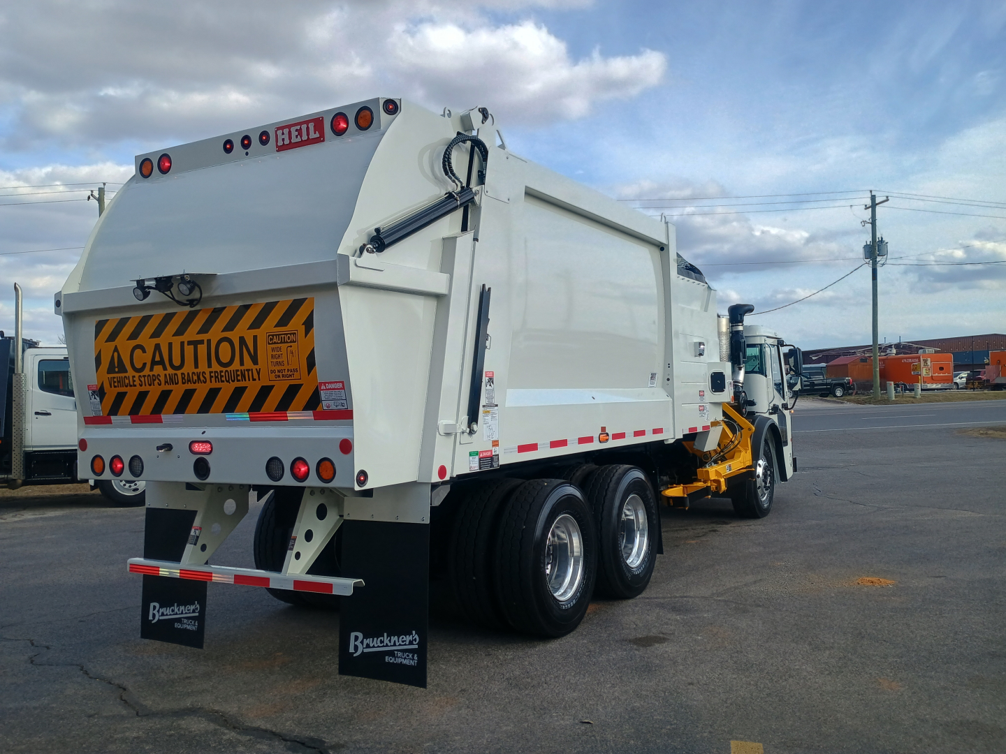 Mack LR64 refuse truck rear-side view showing rear dump body with caution sign, dual rear axles, and side loader truck chassis.