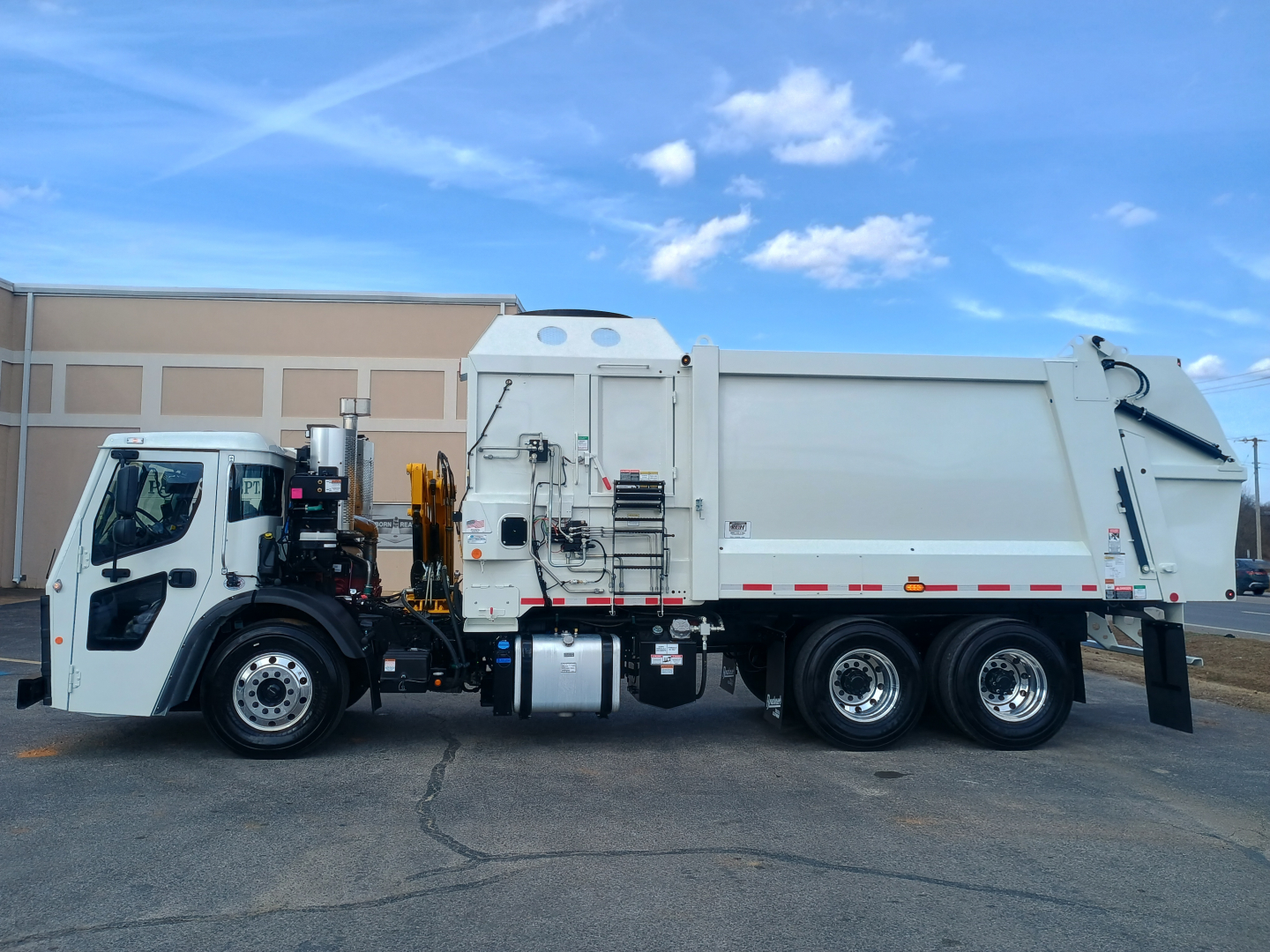 2026 Mack LR64 refuse truck side view showing cab and large white dump body with hydraulic arm and storage compartments