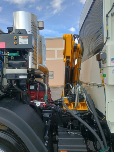 Mack LR64 engine bay showing diesel engine and hydraulic components with yellow chassis crane arm on the side.