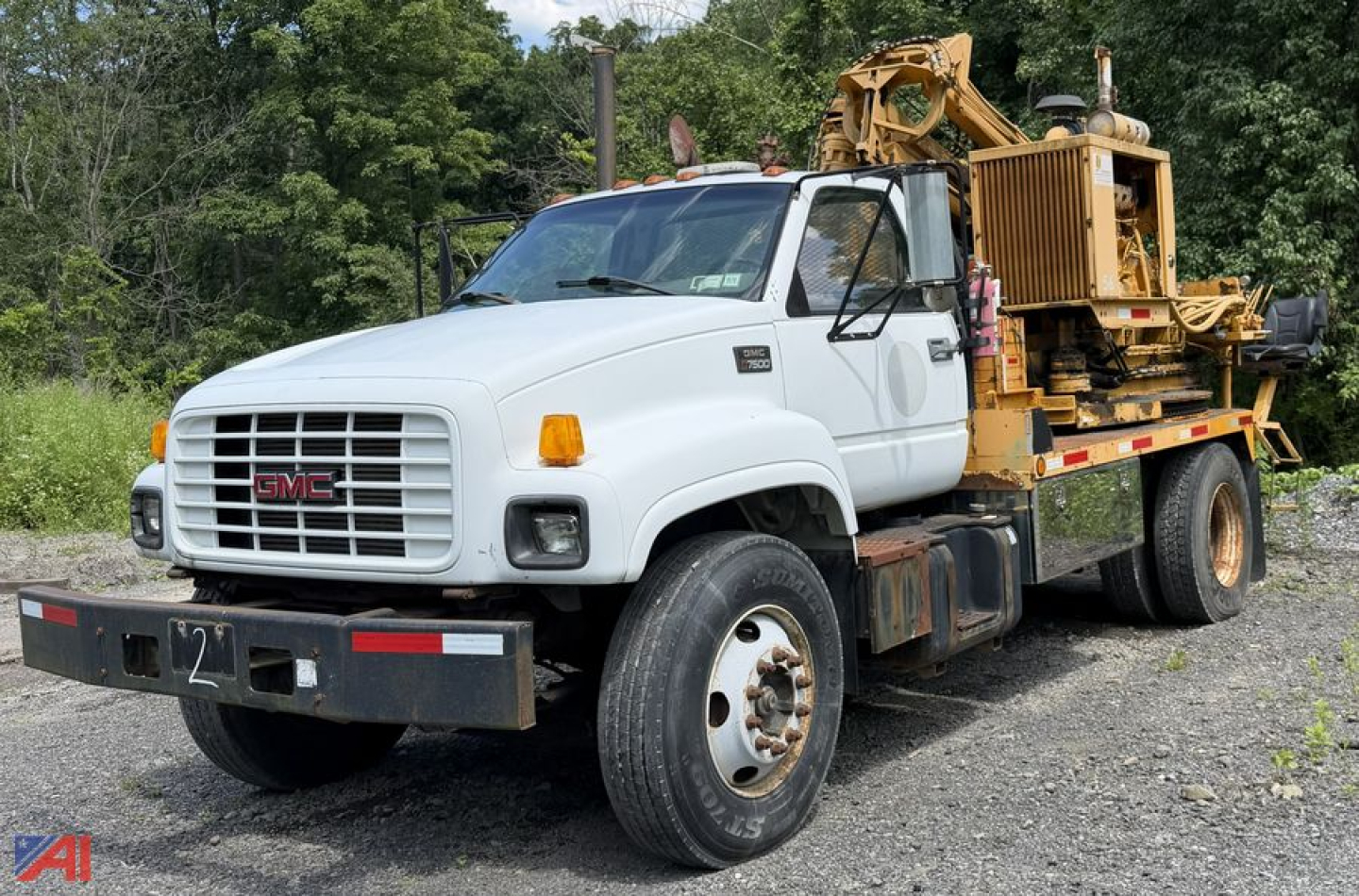 GMC C7500 utility truck with a flatbed and equipment on back, white cab, front grille with GMC badge, visible side mirror, orange turn signals, working ground clearance.