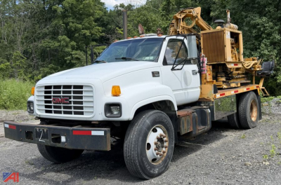 GMC C7500 utility truck with a flatbed and equipment on back, white cab, front grille with GMC badge, visible side mirror, orange turn signals, working ground clearance.