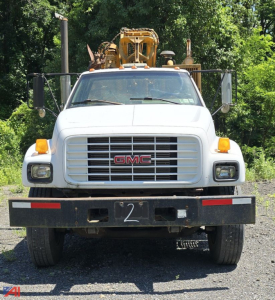 Front view of a white GMC C7500 utility truck with a heavy bumper, large grille, and yellow lights; number plate shows '2' on the bumper.