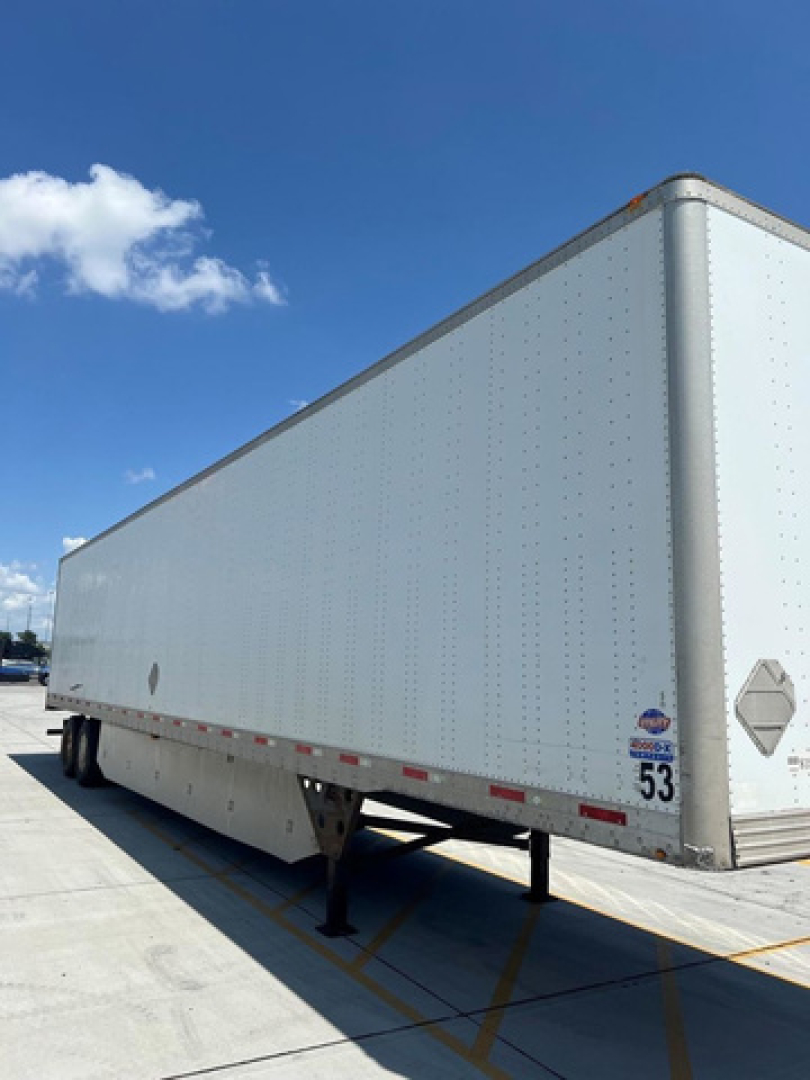 Trailer body of a 2014 utility van/trailer showing a long white corrugated side, diamond plate ramp area, and support legs at the front with a blue sky background.