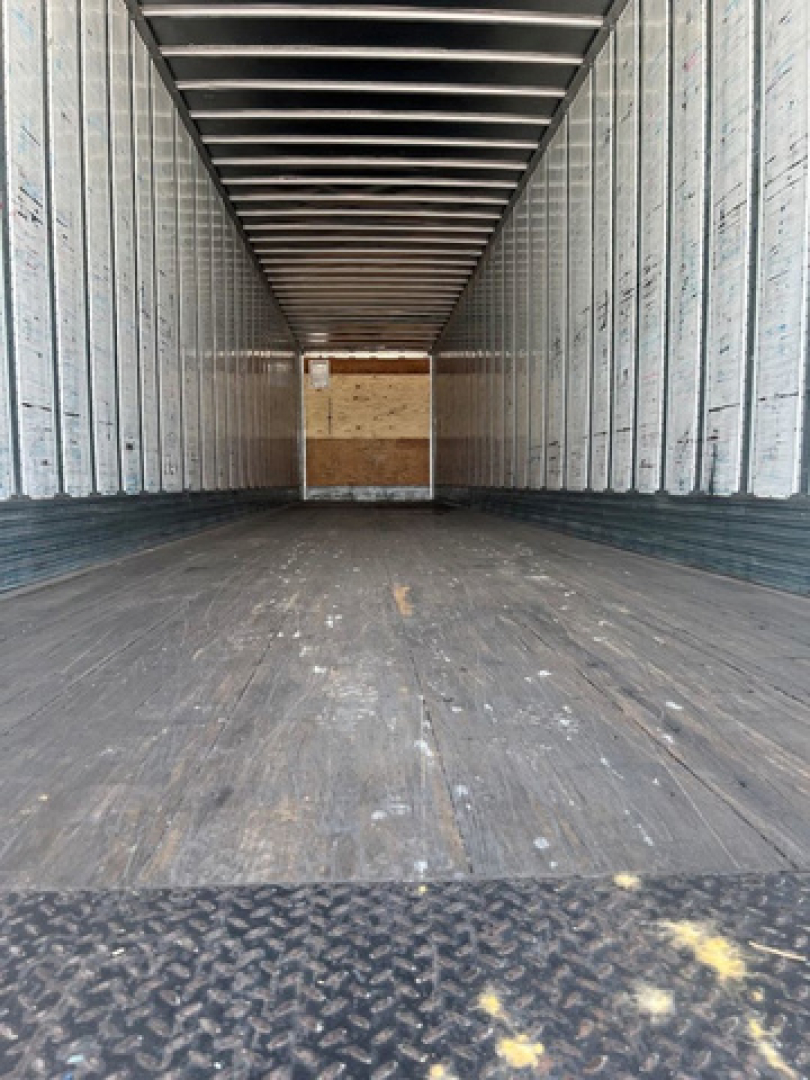 Trailer interior of a 2014 utility van showing empty cargo bay with metal sidewalls and wooden rear door.