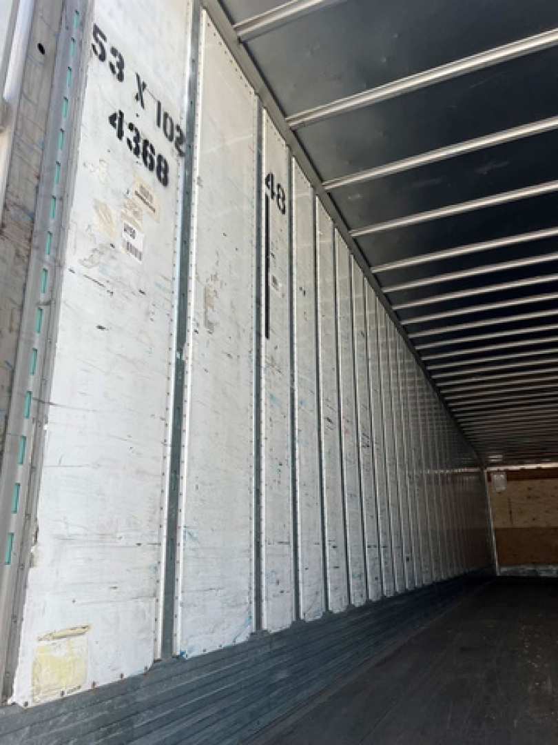 Trailer interior with metal panels and overhead ribs; faint printed numbers along wall including '53 X 1032' and '41866' and various stickers.