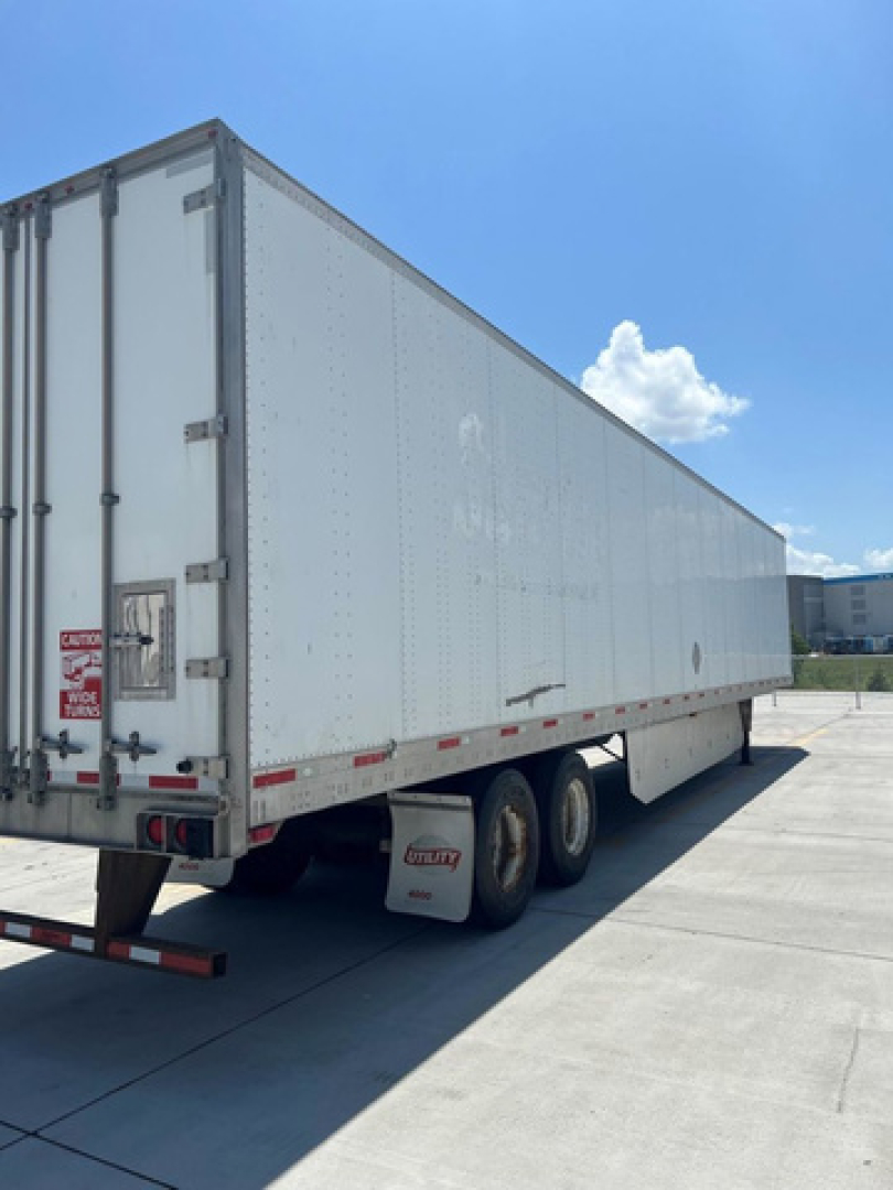Utility van trailer in side and rear view showing white exterior, tandem axles, and back doors.