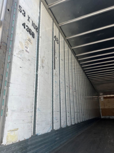 Trailer interior with metal panels and overhead ribs; faint printed numbers along wall including '53 X 1032' and '41866' and various stickers.