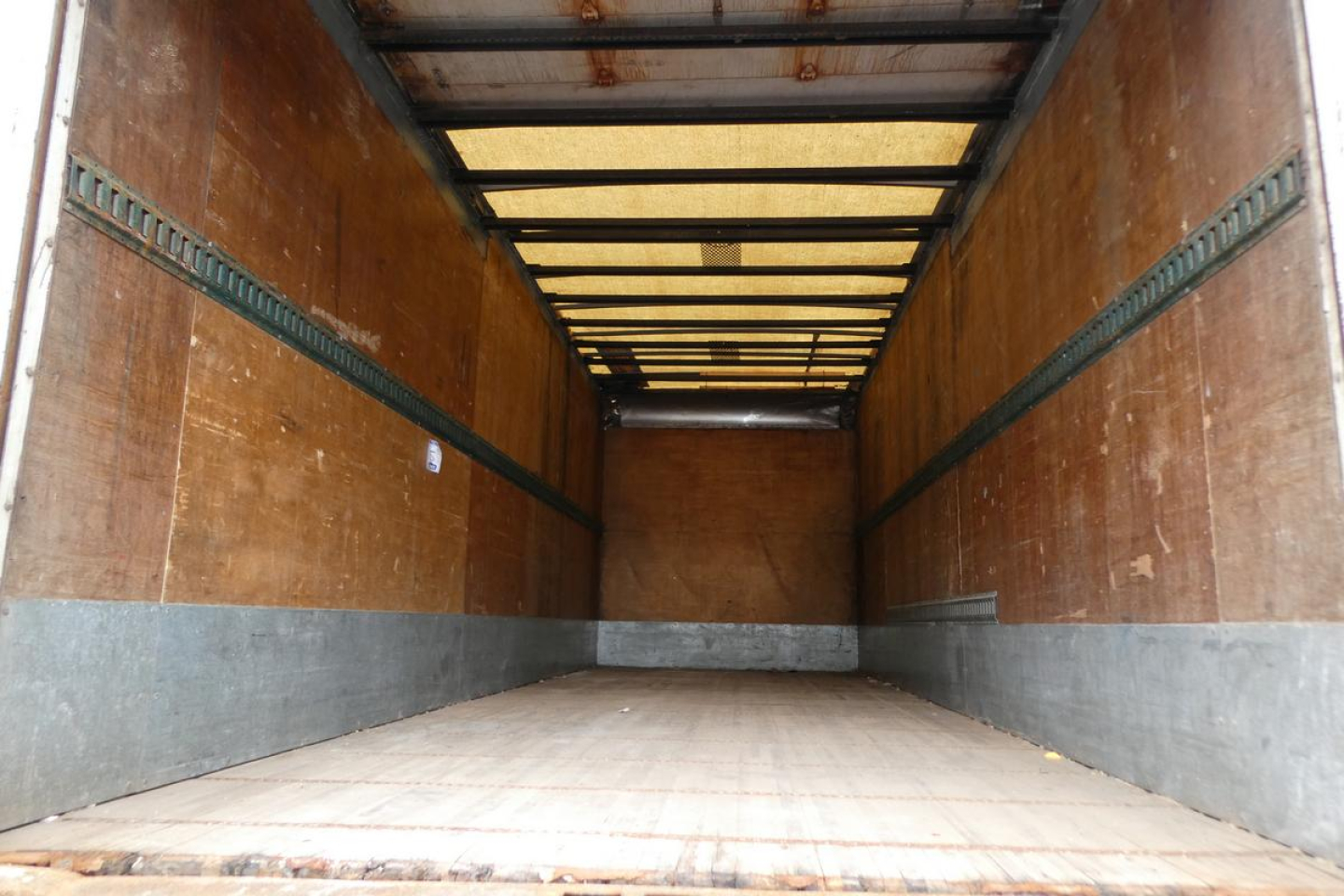 Truck trailer interior showing empty cargo area with wood panel walls and metal tracks.