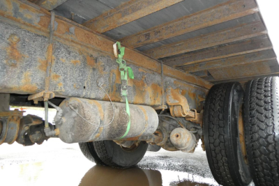 Underbody view of a 2006 Sterling ACTERRA box truck showing the drive axle and suspension components, rust-toned frame, and a green strap securing a cylindrical component.