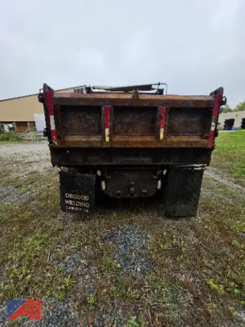Back of dump truck with plow attachment showing taillight assemblies, rusty bed, and a black mudflap with white lettering (reading 'OSGOOD VELDING ???').