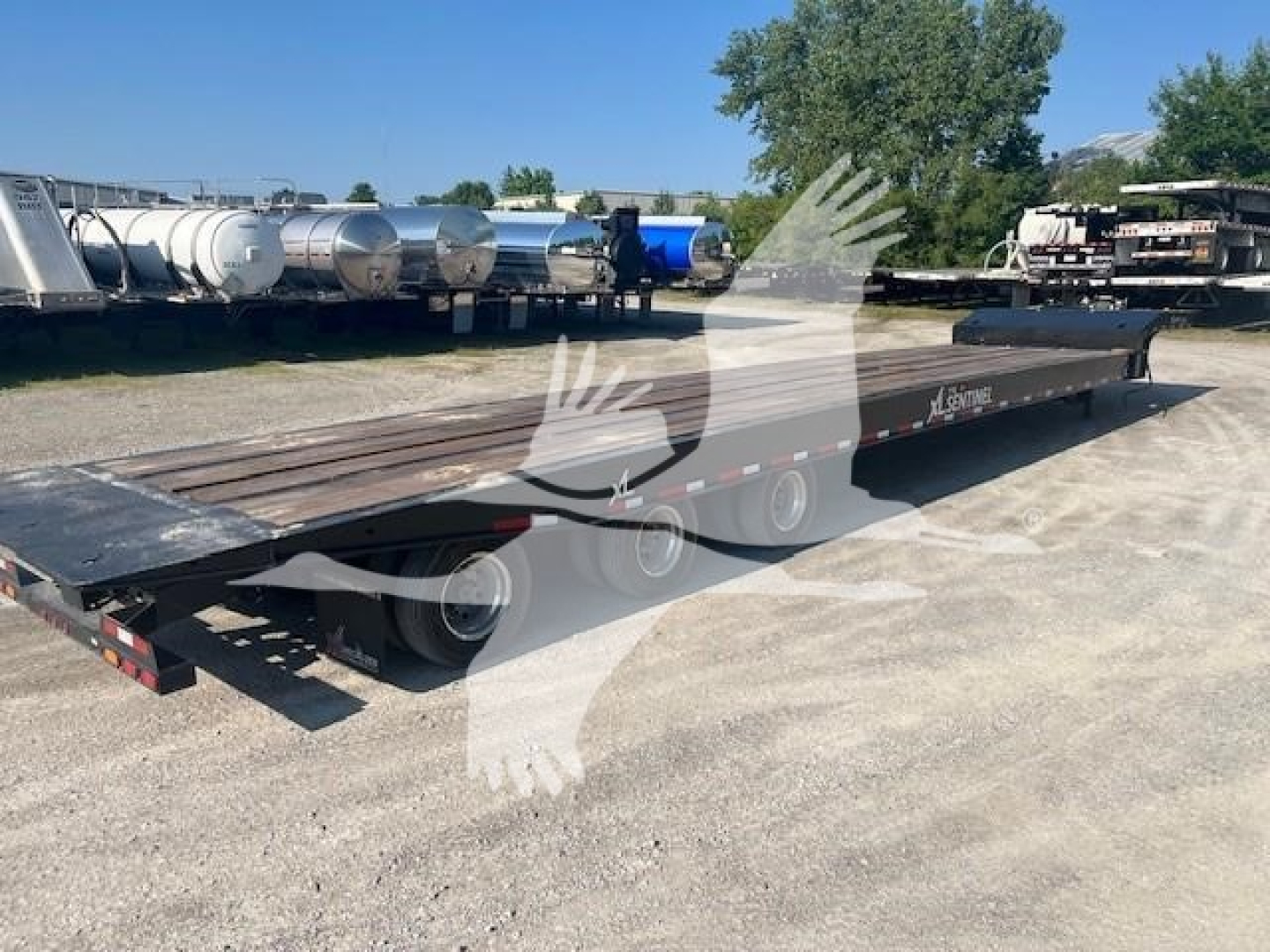 Trailer showing flatbed with low profile, dual rear axles and long deck in an open lot.