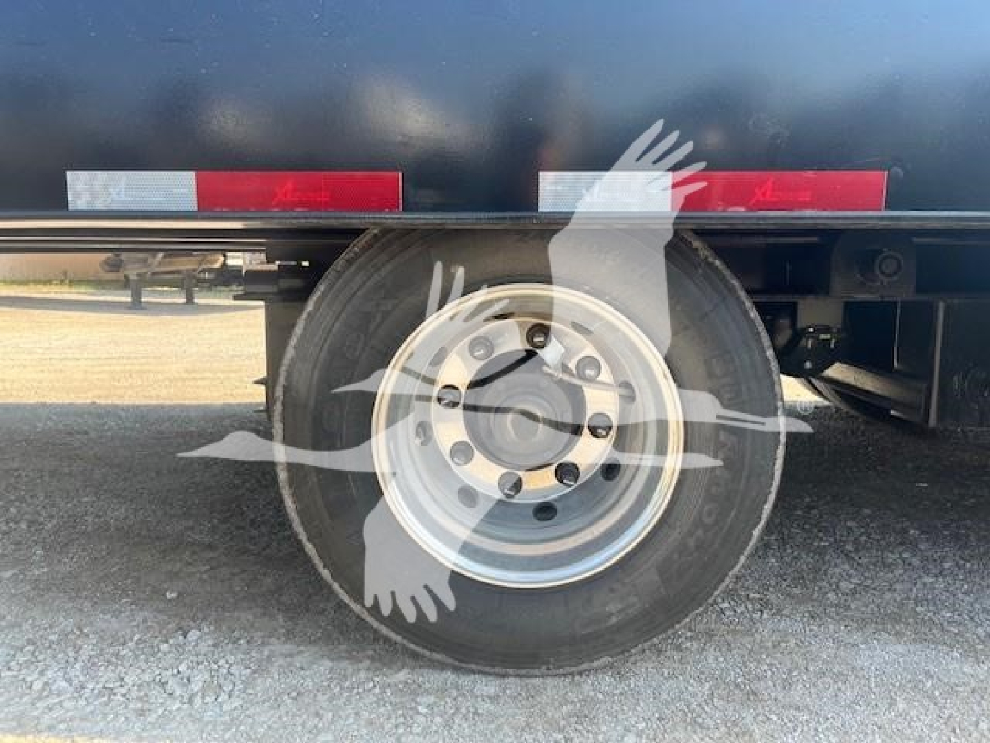 Trailer wheel and tire on travel axle trailer showing steel wheel and tire tread with surrounding gravel.