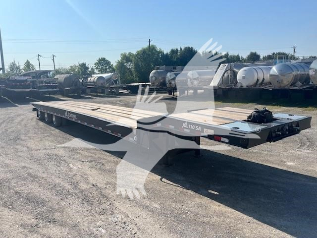 XL Specialized 110SA trailer in a lot showing long flatbed with dual tandem axles and loader ramp at front, text XL110SA near hitch.