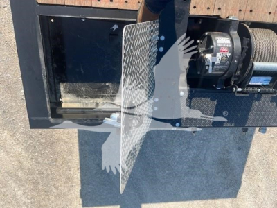 Trailer component with a winch motor and a metal diamond-plate guard, showing part of a trailer frame and equipment.