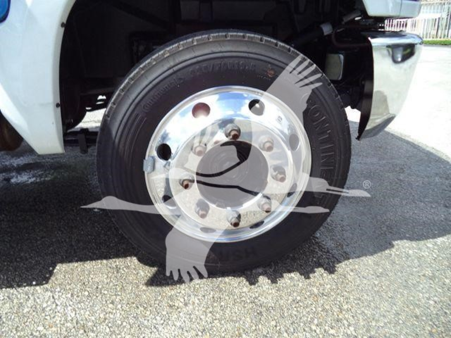 Front wheel of a 2023 Chevrolet Silverado 6500HD truck showing steel wheel with lug nuts and black tire; partial white body panel visible.