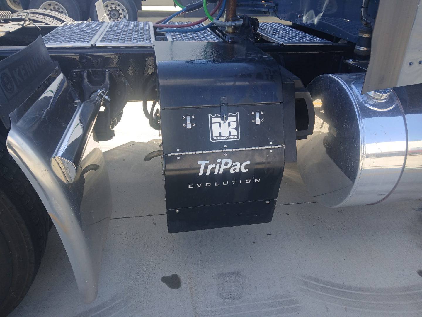 Kenworth W900L truck chassis showing TriPac Evolution battery/auxiliary power unit enclosure with exhaust and fuel tanks visible.