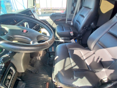 Kenworth W900L truck interior showing steering wheel, driver seat, and front passenger seat with dash area and floor mats visible.