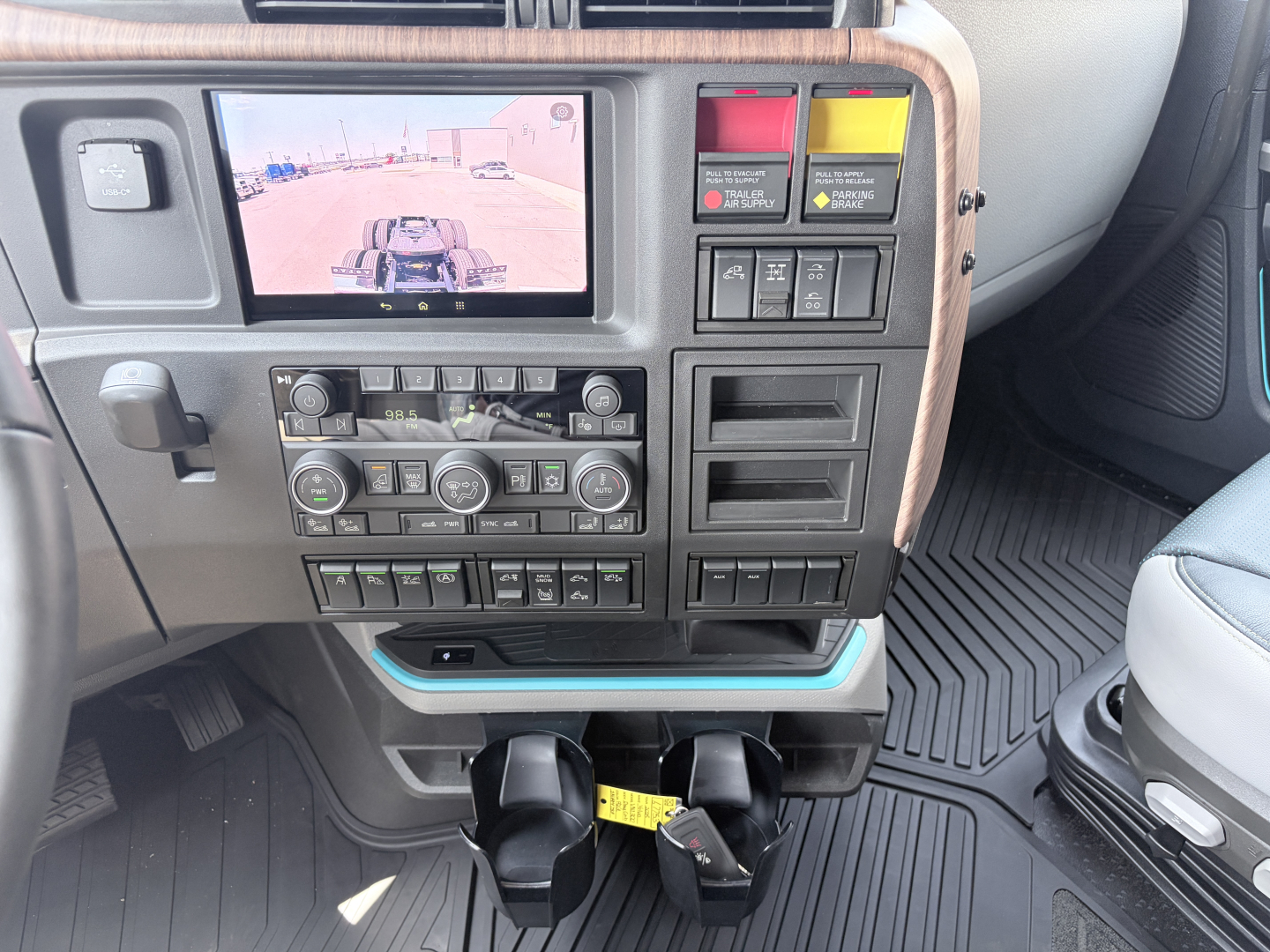 Volvo VNL dash area showing rear-view camera display and control panel with climate controls, switches, cargo light, and cupholders in a new truck.