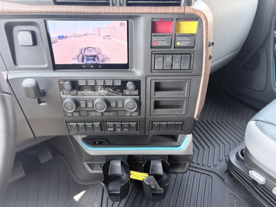 Volvo VNL dash area showing rear-view camera display and control panel with climate controls, switches, cargo light, and cupholders in a new truck.