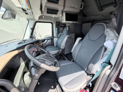 Truck cab interior in view showing driver seat and dashboard with large steering wheel and overhead compartments.