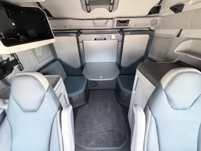  Volvo VNL cab interior with front seats, sleeper area, table, and storage compartments visible.