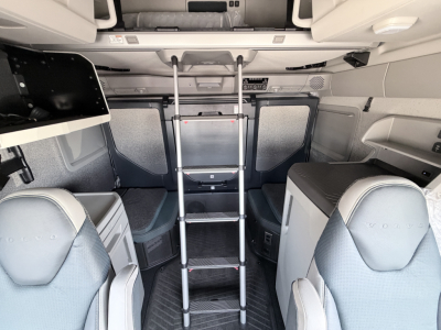 Interior view of a Volvo VNL64T860 cab with a foldable ladder extending from the sleeper area, storage compartments, and light gray upholstery visible.