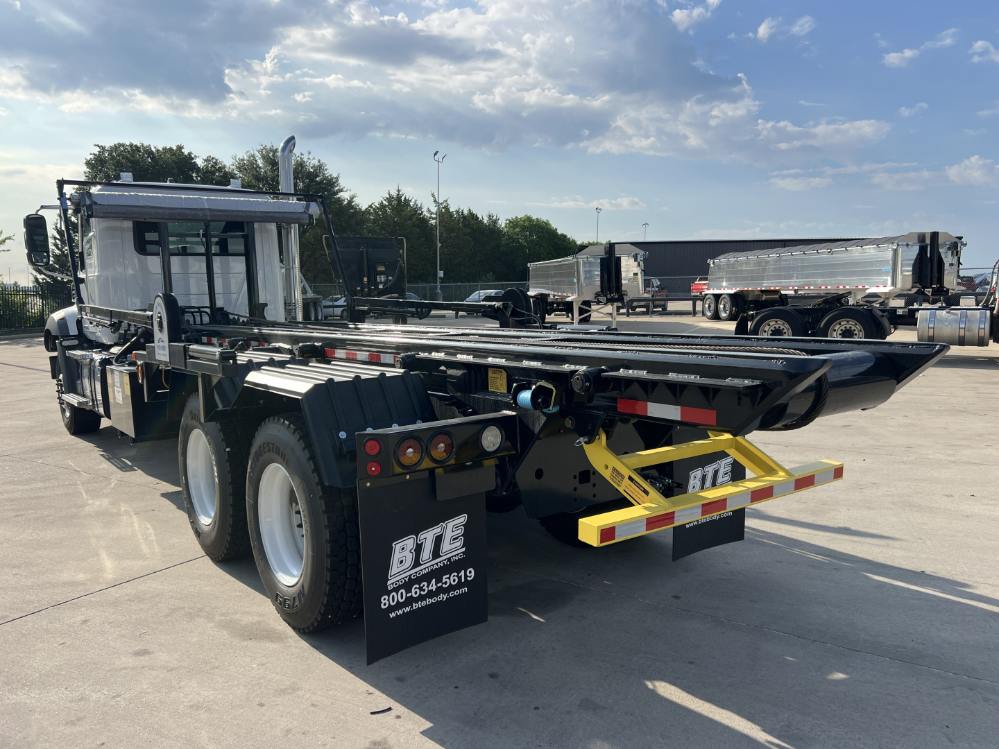 Rolloff truck chassis showing rear view with platform and dual rear axles, BTE mud flaps with contact number, yellow hitch components, and Mack GR64B spec details not visible in image.