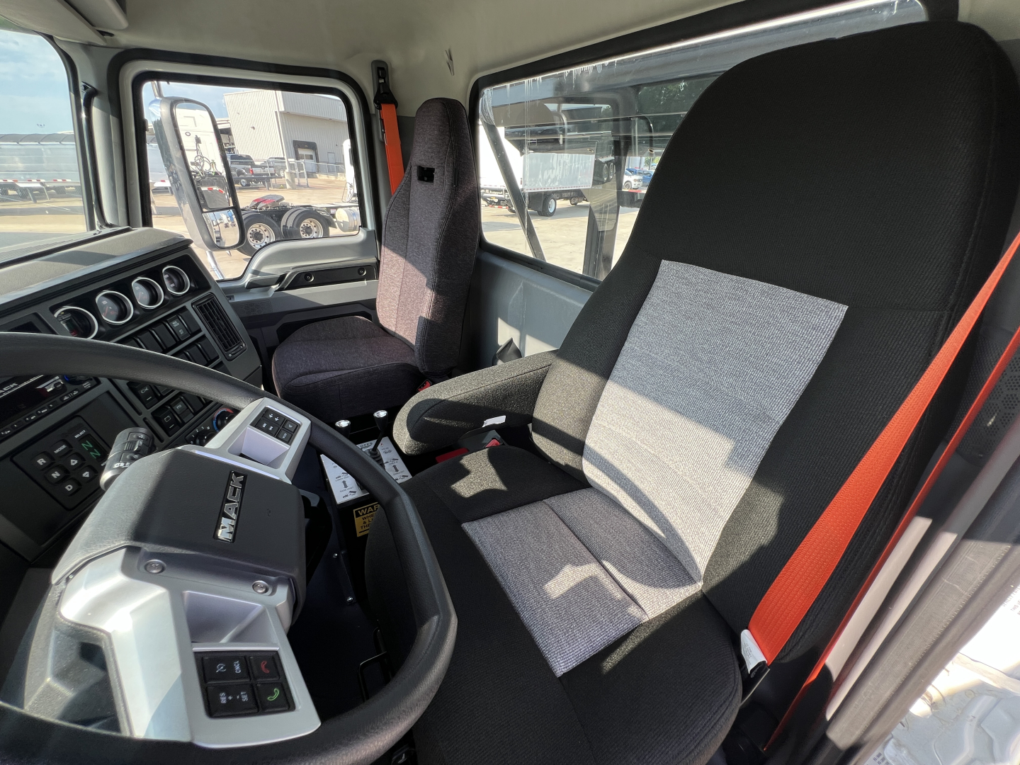 Interior of a Mack GR64B roll-off truck cab showing steering wheel, dashboard gauges, driver seat, and seat belt in view.
