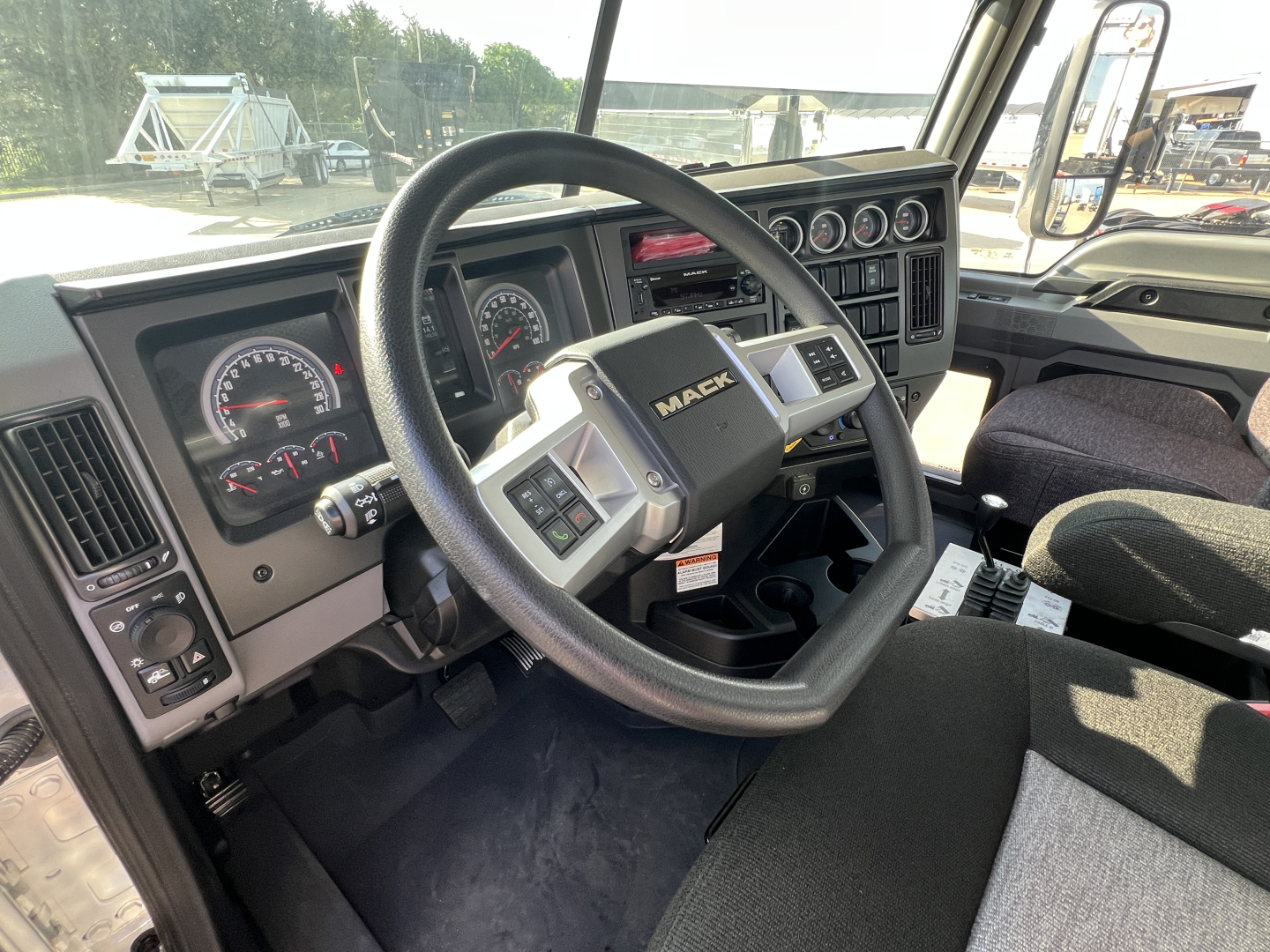 Mack GR64B truck interior showing steering wheel with Mack logo, instrument cluster, and dashboard controls.