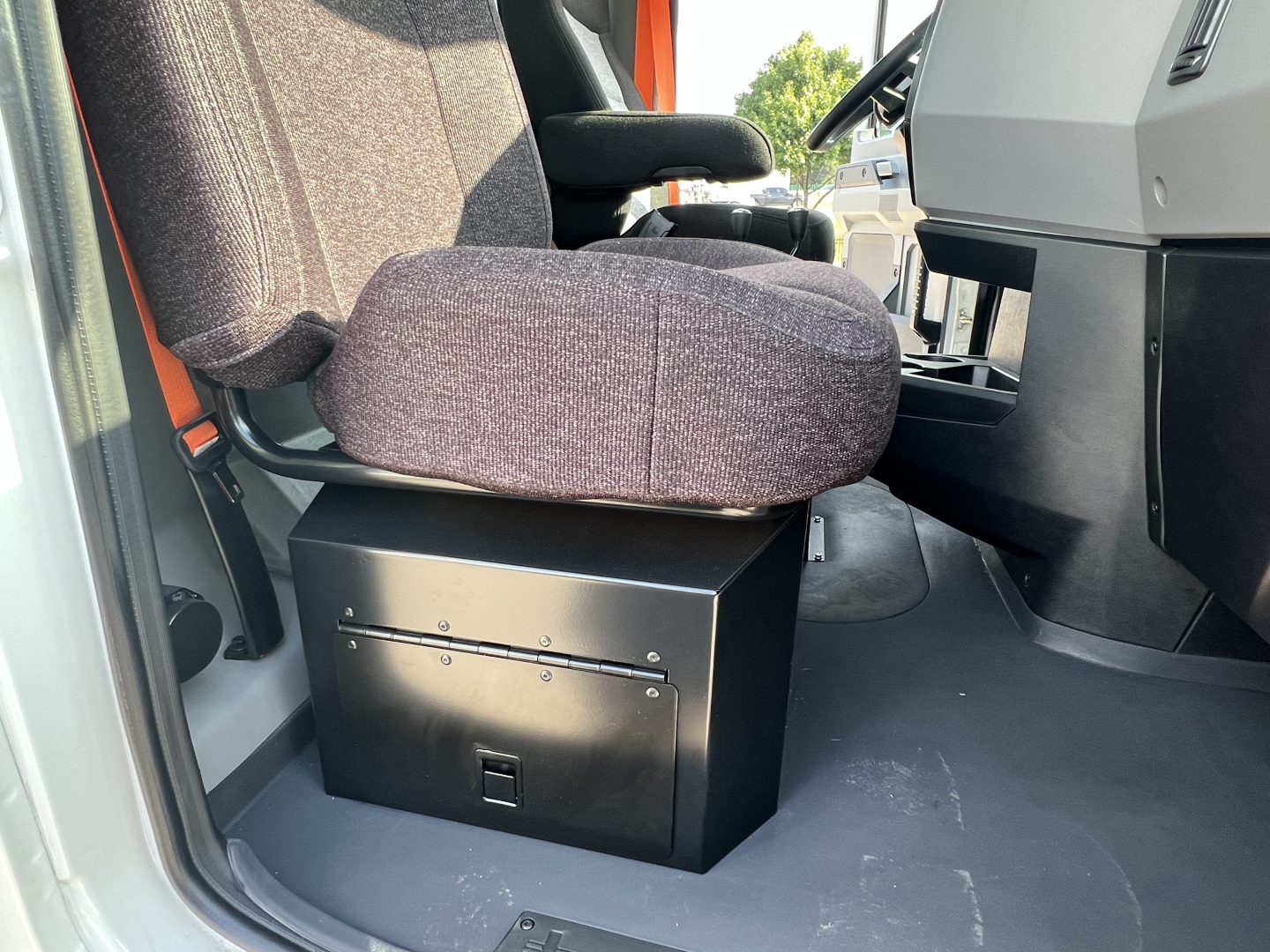 Mack GR64B cab interior with a black storage console under the driver seat and a pinkish fabric seat cushion visible.
