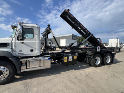 Mack GR64B rolloff truck side view showing hydraulic loading arms and chassis components.