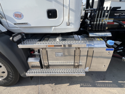 Truck side view showing diamond plate steps and metal toolbox under cab with labels and stickers.
