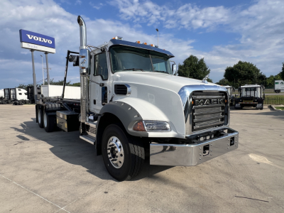 Mack GR64B truck in a dealership lot showing front grille, chrome bumper, and side exhaust stack with Volvo sign in background.
