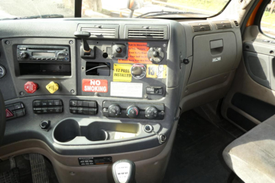 Truck cab dashboard showing control switches, gauges, and badges with no smoking sign and sticker labels.