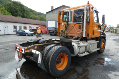 Orange Freightliner Cascadia 125 daycab tractor cab rear and left side with missing door panel showing chassis and fuel tanks.