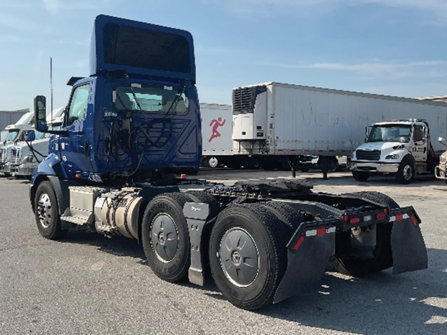 Truck cab and chassis of a blue 2020 International RH613 daycab with dual rear axles and a white trailer in background.