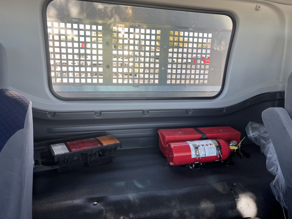 Isuzu FTR truck interior cargo area with a red fire extinguisher and a black toolbox, metal grid window behind.