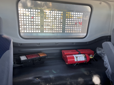 Isuzu FTR truck interior cargo area with a red fire extinguisher and a black toolbox, metal grid window behind.