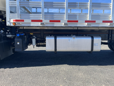 Isuzu FTR truck side view showing large rectangular aluminum fuel tank under the flatbed with straps, rear of cab and wheel area not visible