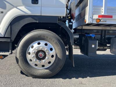 Isuzu FTR front wheel well and side of stake bed truck showing large single rear wheel and fuel/air reservoirs; view includes wheel, tire, fender, chassis and underbody components.