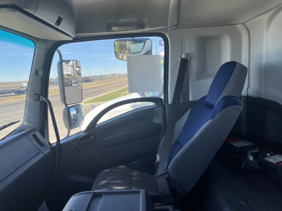 Isuzu FTR truck interior cabin front seats and dashboard visible with blue-and-gray seat upholstery, steering wheel, side window mirror, and driver seat belt.