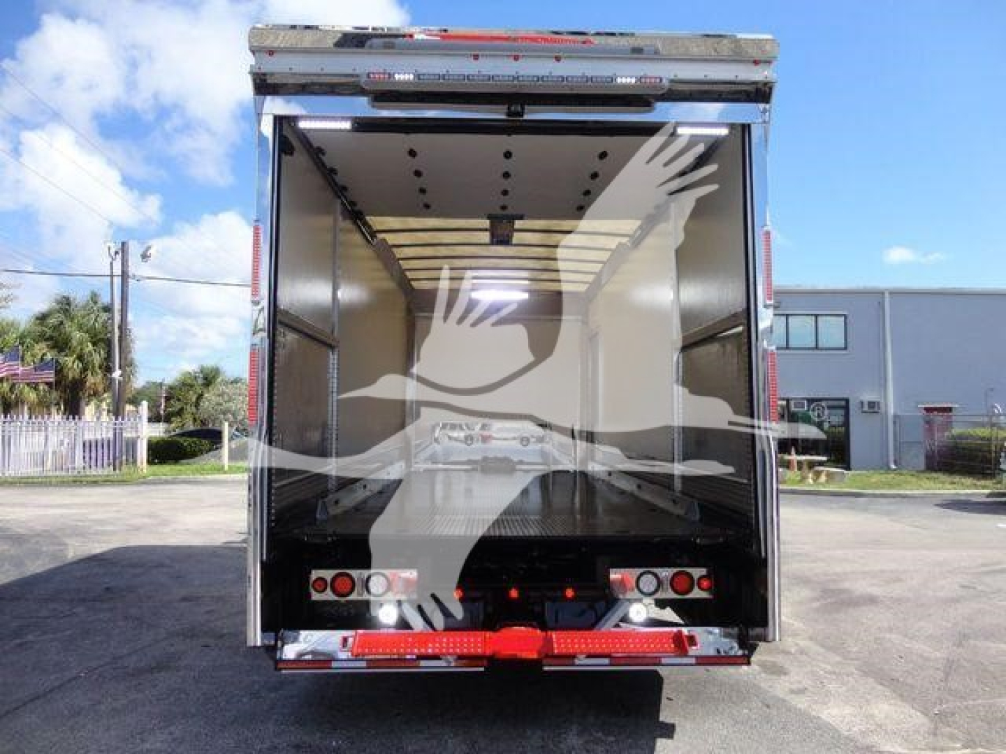 Rear view of a new Mack MD6 rollback truck with open cargo area showing interior panels and rear lights.