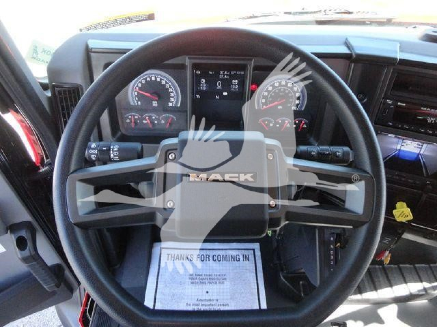 Steering wheel and instrument cluster of a 2027 Mack MD6 cab interior, showing Mack-branded steering wheel and dashboard gauges.