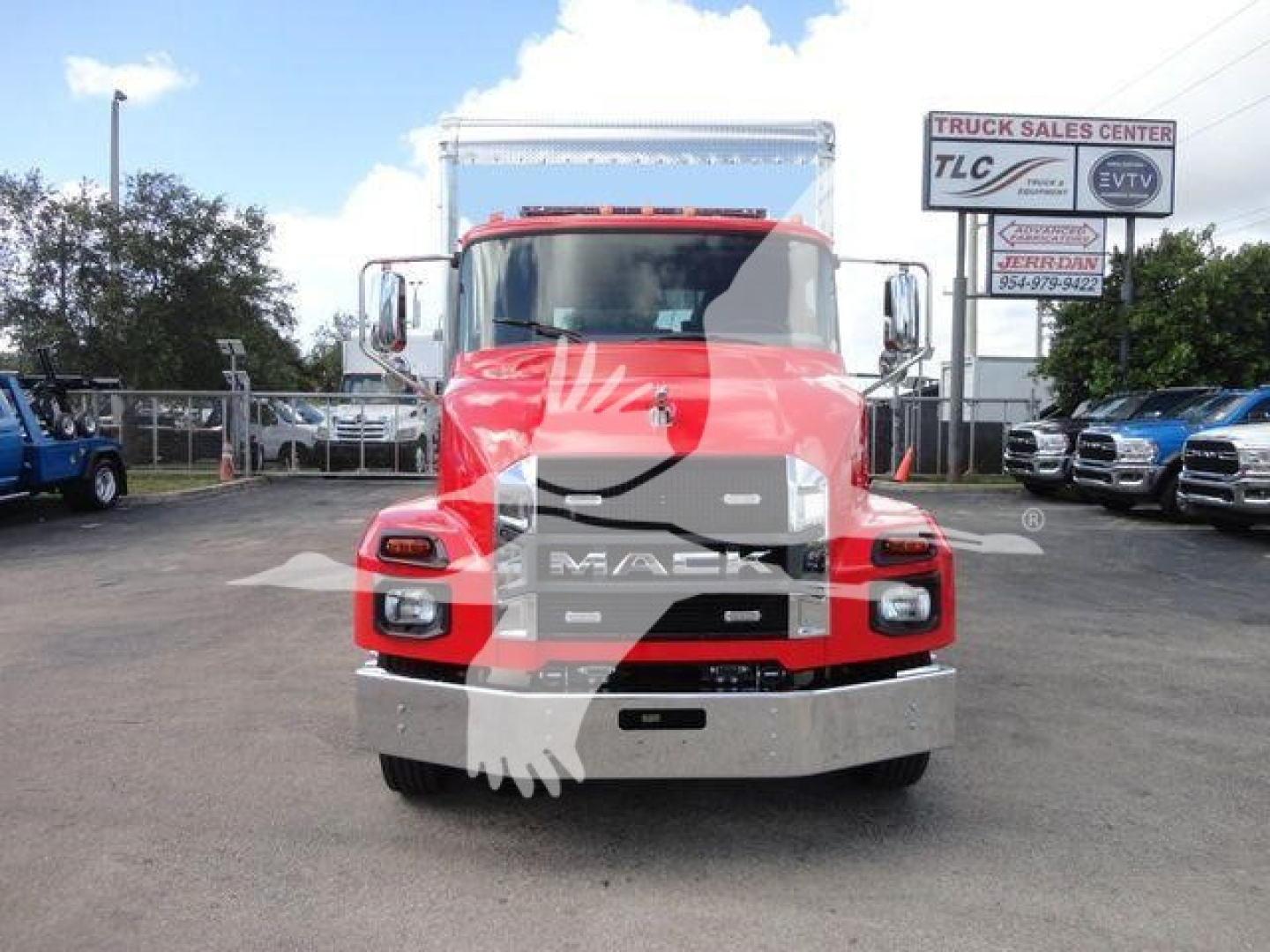 MD6 Mack rollback truck front view showing large chrome grille with MACK letters and bumper, red cab with silver accents, side mirrors, and dealership lot in background.