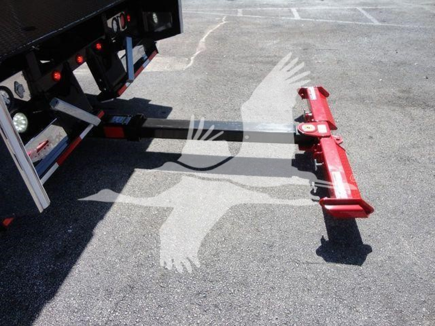 Mack MD6 rollback truck hitch attached to a trailer, red hydraulic arm at the end, with a steel hitch bar extending from a black trailer frame.