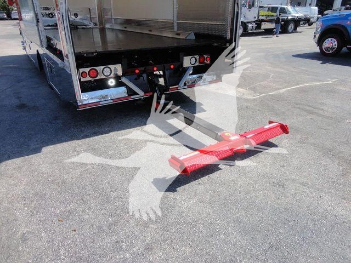 Rear view of a 2027 Mack MD6 rollback truck with a red tow hook attachment on the ground near the chassis.